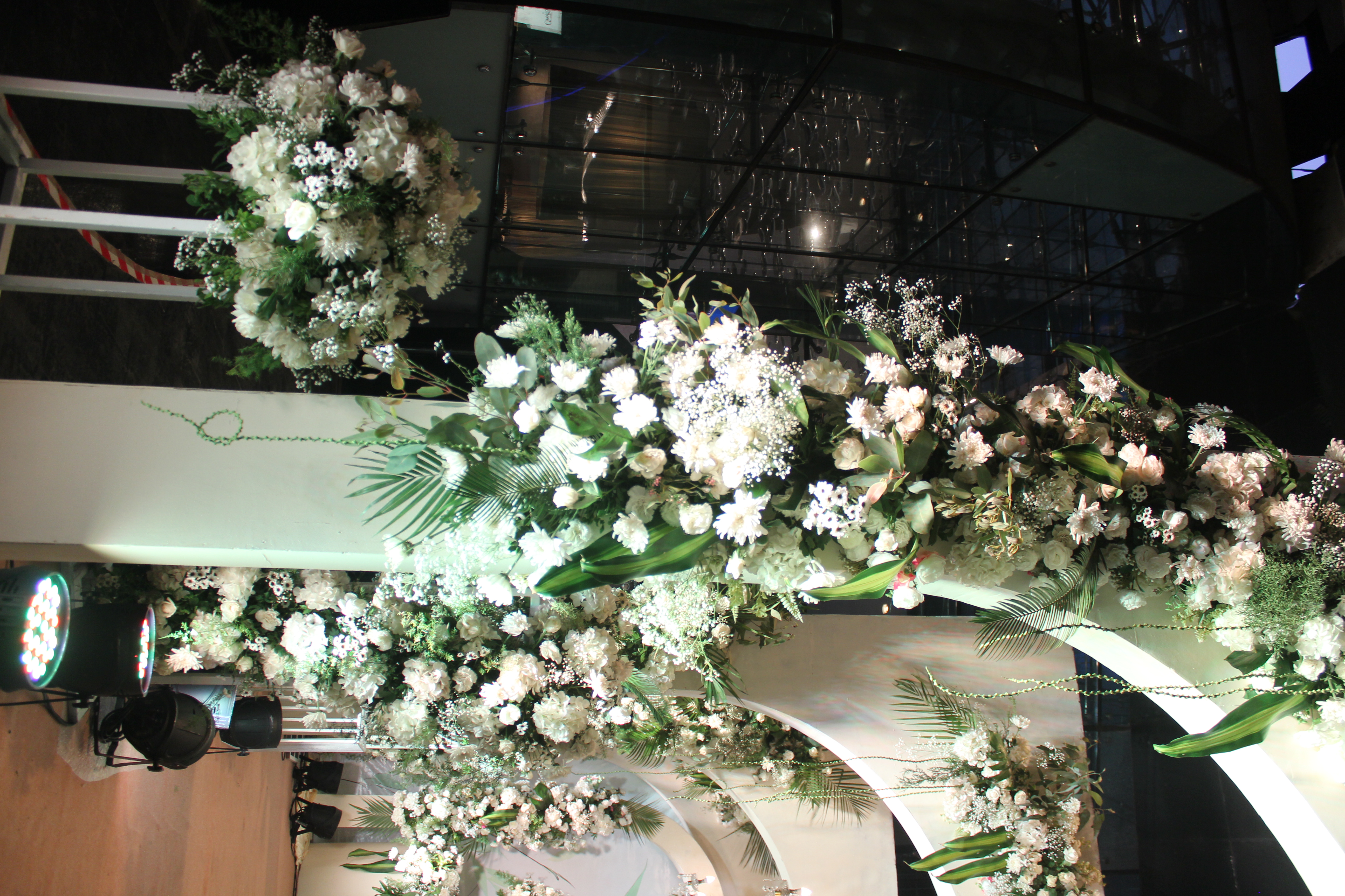 White blooms and palm fronds on a floral arch, close