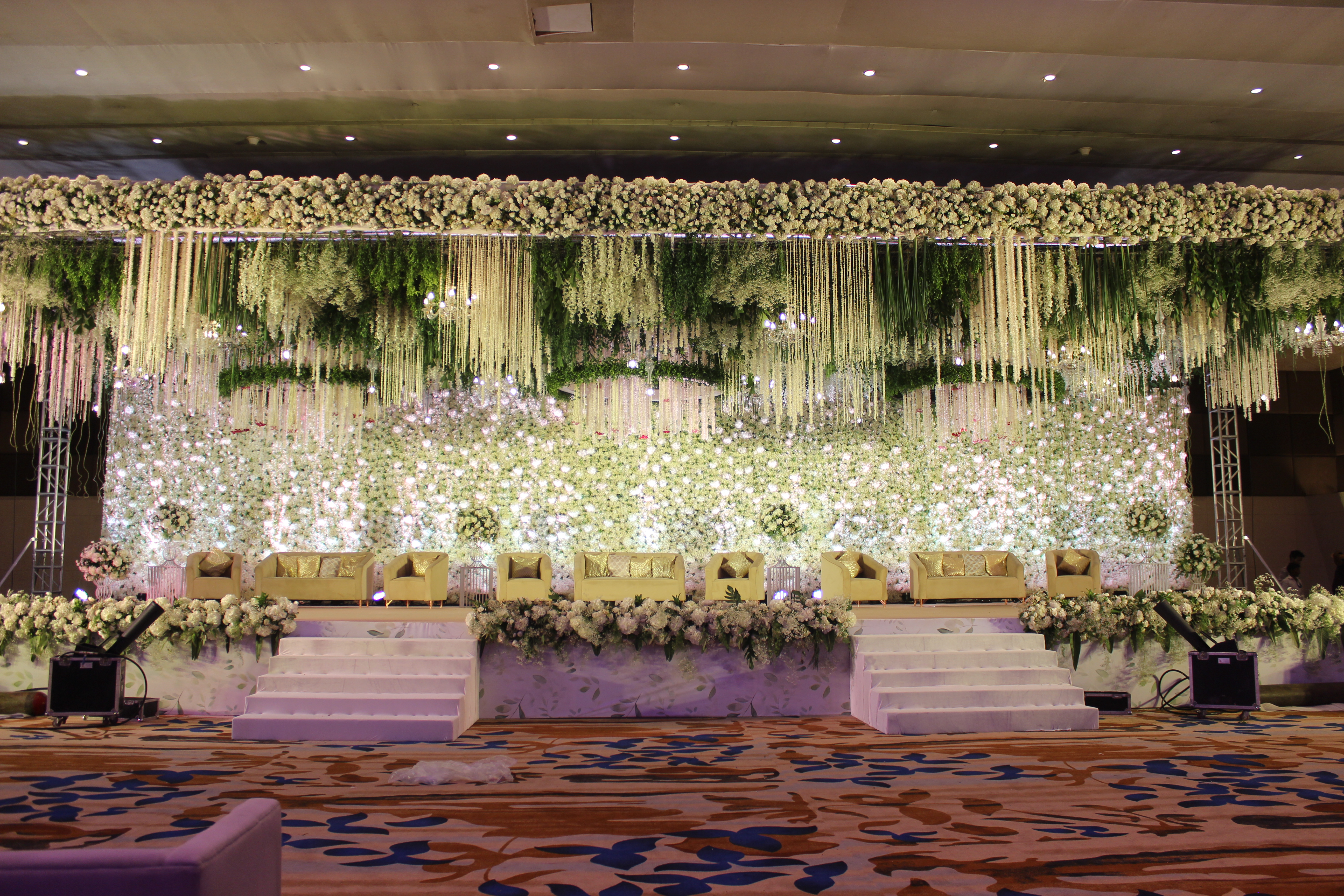 A white floral stage built by Arika Event, pendant blooms above a lit floral wall