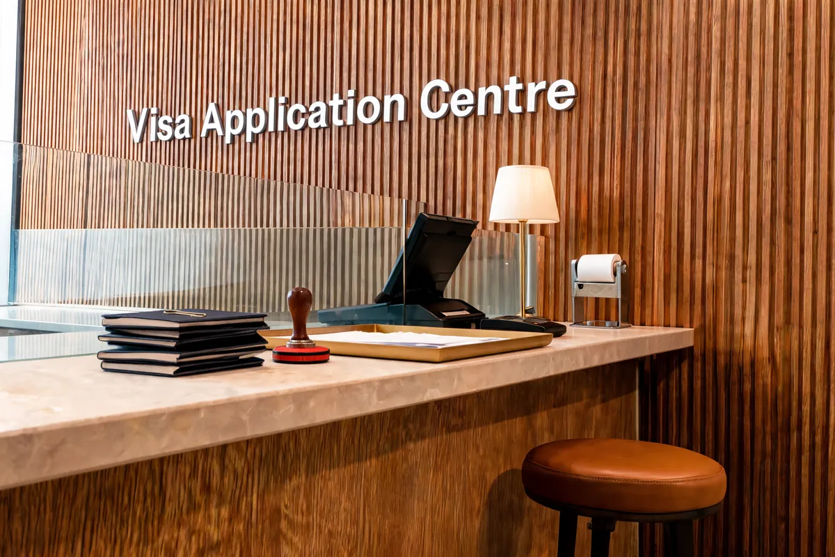 A visa application centre counter in stone and fluted walnut, passports stacked beside a stamp